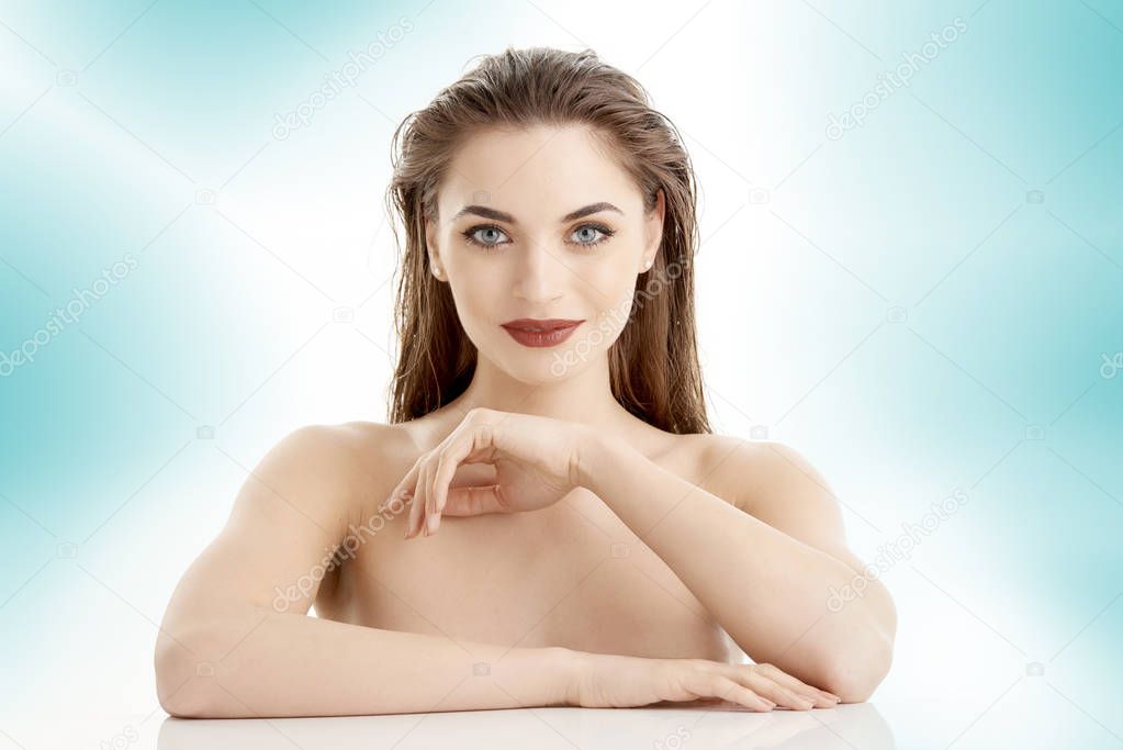 Smiling young woman wearing dark lipstick and eyeliner while posing at isolated light blue background.
