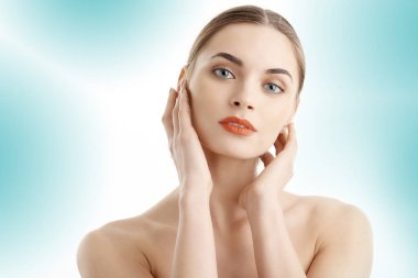 Stüdyo kameraya izole açık mavi renkli poz süre seyir mükemmel cilt yüz güzel bir genç bayan bir kadeh. Ona dokunmayı face whit elleri. 