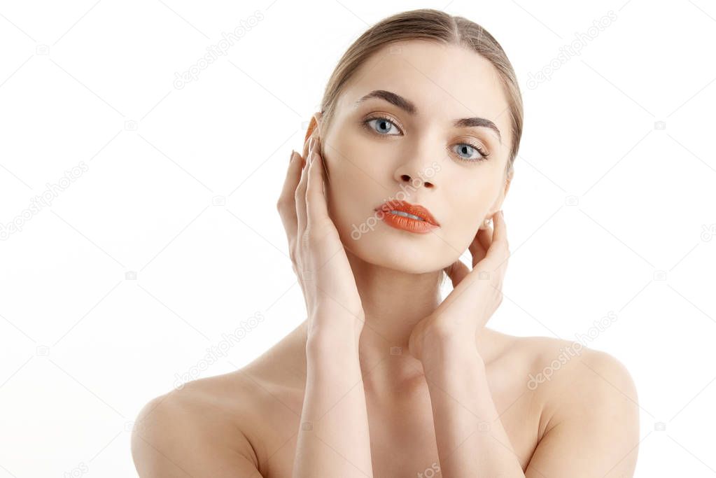 Beautiful young woman with clear perfect skin and with red lipstick looking at camera while posing at isolated white background. Amazing female touching her face with her hands. 