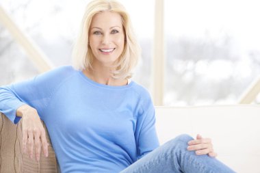 Kanepede oturan ve evde rahatlatıcı güzel gülümseyen kadın. 