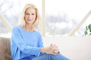 Kanepede oturan ve evde rahatlatıcı güzel gülümseyen kadın. 