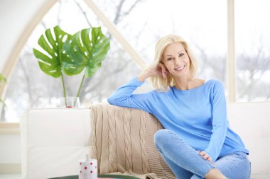 Kanepede oturan ve evde rahatlatıcı güzel gülümseyen kadın. 