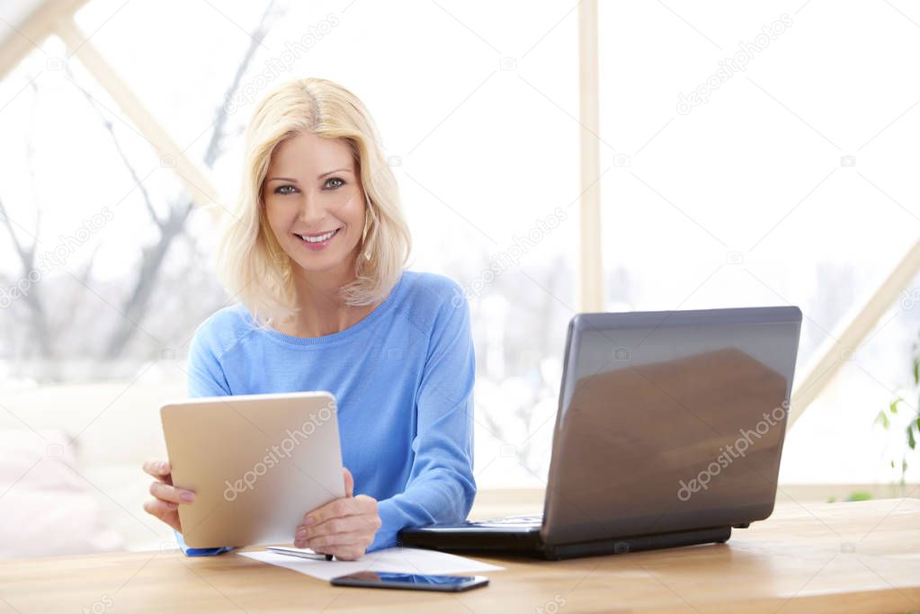 Close-up of smiling businesswoman holding digital tablet in her hand while sitting at desk and working from home.