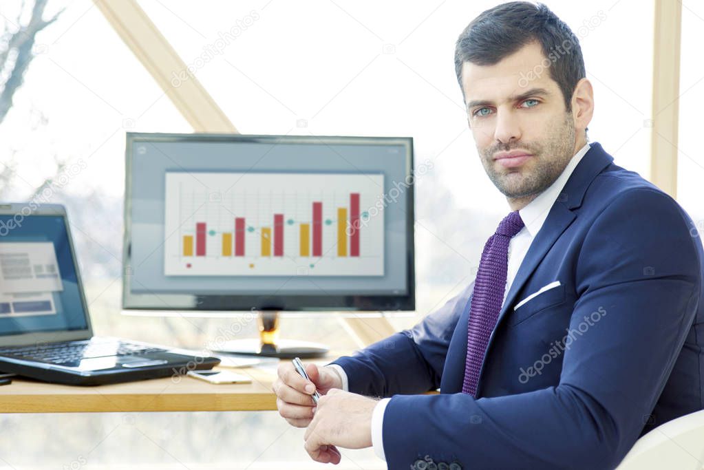 Portrait of young financial assistant businessman wearing suit while sitting at office desk and working on financial report. 