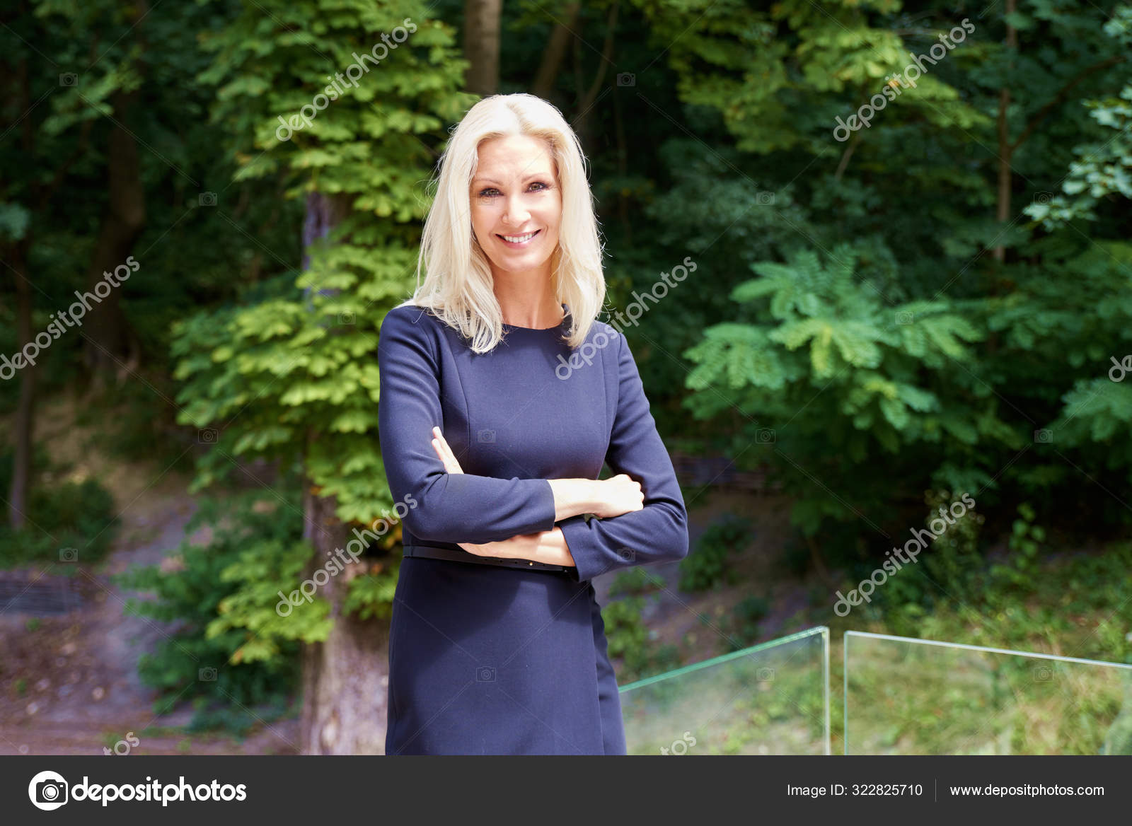 カメラを見ながら外を横切り笑顔で腕を組んで立つ上品な熟女のポートレート ストック写真 C Sepy