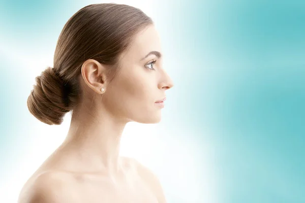 Woman face profile shot. Beautiful young woman with perfect skin looking away while standing at isolated light blue background.