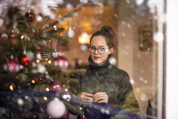 窗外飘雪时装饰圣诞树的可爱女人的画像 — 图库照片