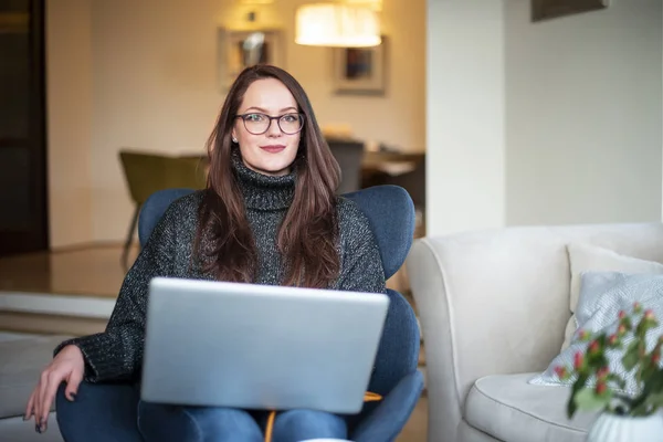 Egy Mosolygó Fiatal Laptopját Használja Miközben Széken Otthonról Dolgozik — Stock Fotó