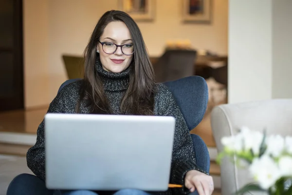 Sırıtkan Genç Bir Kadının Dizüstü Bilgisayarı Ile Sandalyede Otururken Evde — Stok fotoğraf