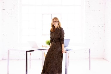 Çekici, gülümseyen orta yaşlı bir iş kadınının ofis masasında dikilirken giydiği elbise.. 