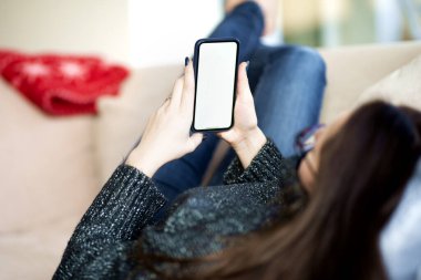 Kanepede dinlenirken, elinde cep telefonu olan genç bir kadının arka plan fotoğrafı..