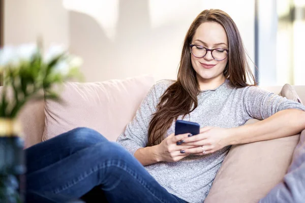 年轻女子在家里沙发上放松时发短信的照片 — 图库照片