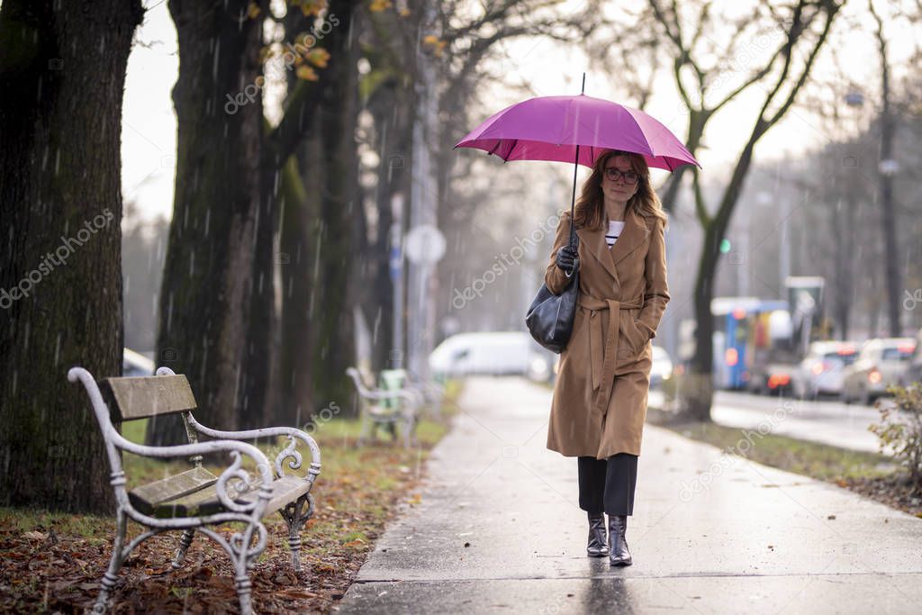 Full length shot of mature woman holding umbrella while walking on the street on a rainy day. 