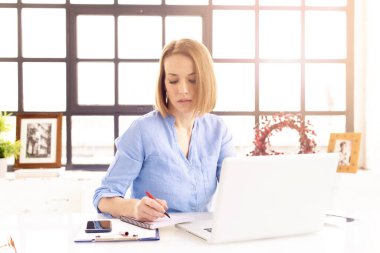 Çekici, olgun bir iş kadınının ofis masasında defterinin arkasında otururken kağıt işleriyle uğraşması..