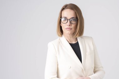İzole edilmiş beyaz arka planda dikilirken gözlük ve ceket giyen orta yaşlı bir kadının yakın plan portresi..