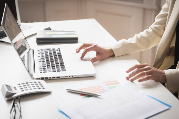 Close-up of financial businesswoman's hand while working on her laptop at office desk.