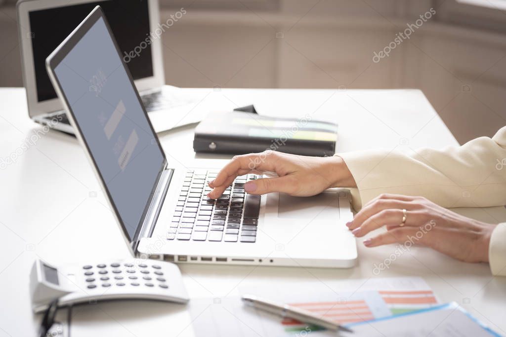 Close-up of financial businesswoman's hand while working on her laptop at office desk.
