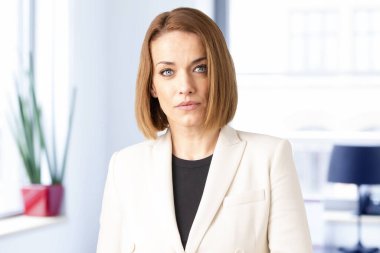 Çekici, orta yaşlı bir kadının, kameraya bakıp gülümserken ceketini giydiği portre resmi.. 