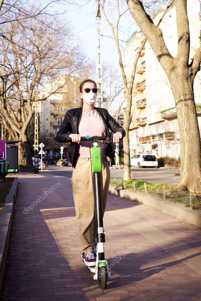 Full length shot of young woman wearing face mask while riding electric scooter in the city.