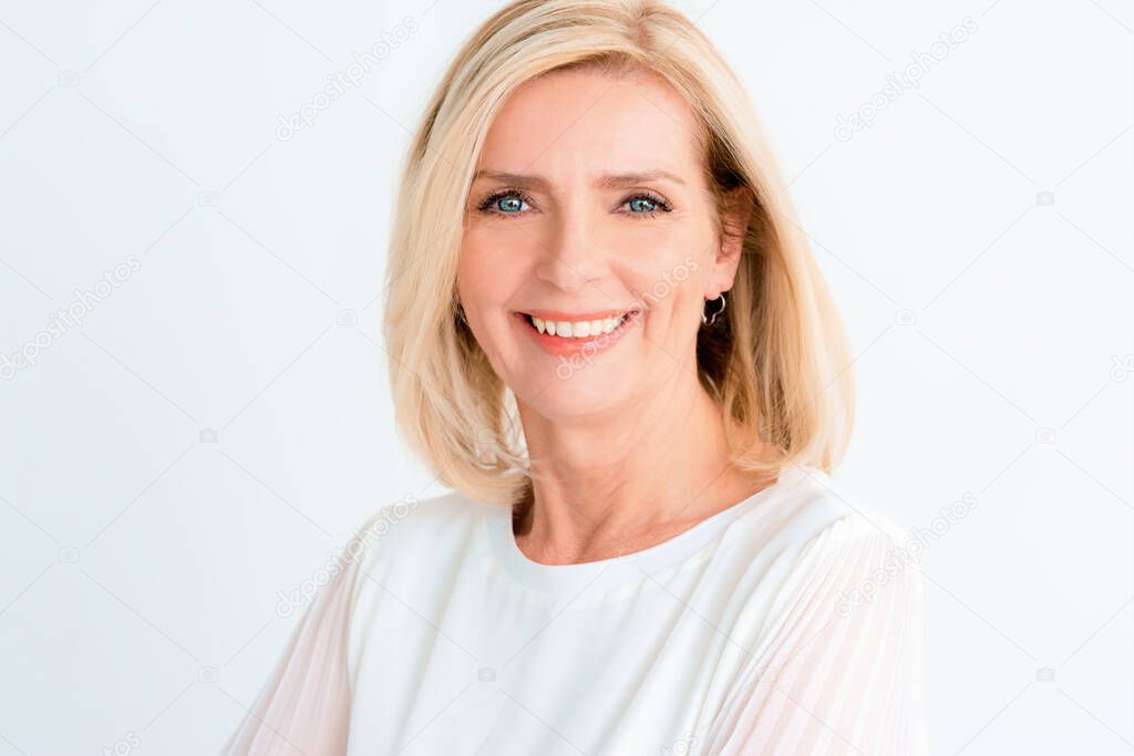 Headshot of beautiful senior woman looking at camera and smiling while standing at isolated white background.