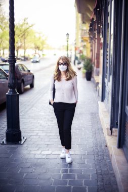 Sokaklarda yürüyen orta yaşlı bir kadının sağlık koruması için solunum maskesi taktığı ve şehirde hızla yayılan koronavirüs salgınının tam boy görüntüsü..