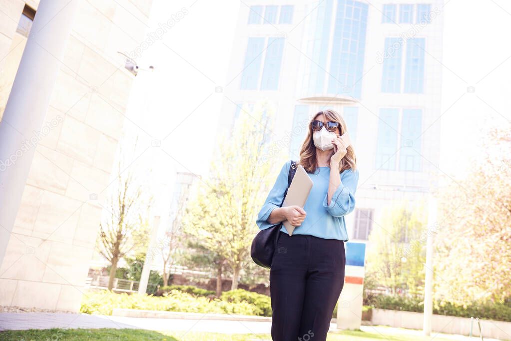 Shot of mature businesswoman wearing a respirator mask device for health protection and making a call while walking on the street. Confident woman wearing face mask while rapidly spreading coronavirus outbreak.