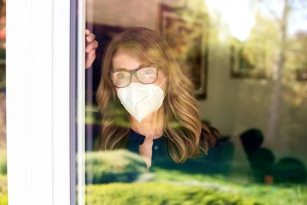 悲伤的女人站在窗边 戴着口罩保护自己不受大流行病的侵袭 这幅阴森森的画像让人毛骨悚然 — 图库照片