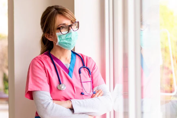 코로나 바이러스가 확산되는 마스크를 돌보면서 창밖을 내다보고 간호사 — 스톡 사진
