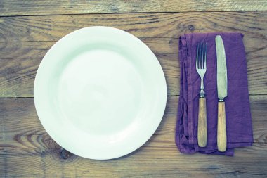 Tahta arka planda çatal bıçak takımı olan beyaz tabak.