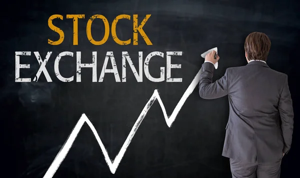 Affärsman skriver börsen på blackboard koncept — Stockfoto