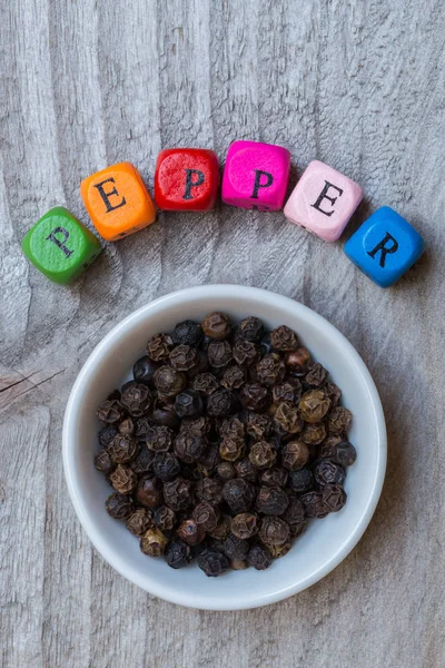 Pepper in bowl with letter cube on wooden background — Stock Photo, Image