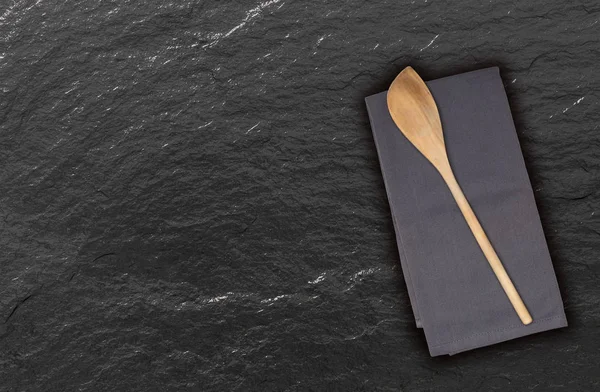 Wooden spoon and kitchen towel on slate — Stock Photo, Image