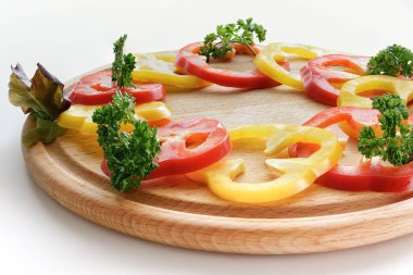 Raw Dilimlenmiş Rad ve sarı dolma biber kompozisyonu ve yuvarlak ahşap kesim tahtasının üzerinde kıvırcık maydanoz yaprakları.