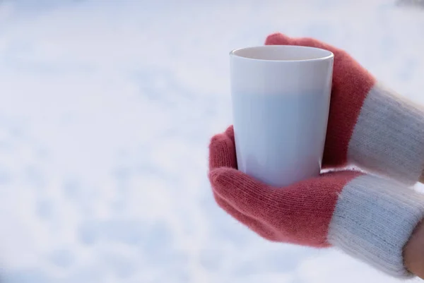 Woman in gloves holding white mug of tea or coffee on snow — Stock Photo, Image