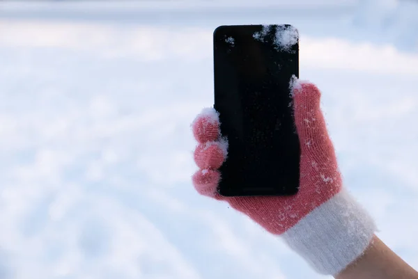 Woman hand in gloves with smartphone in snow on it