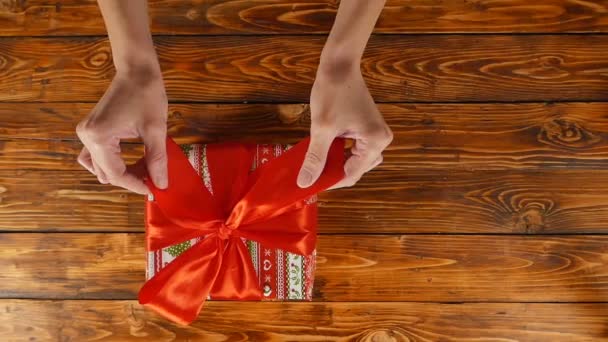 Девушки руки открывают подарочную коробку с красной лентой, вид сверху, замедленная съемка — стоковое видео
