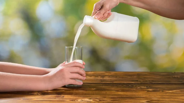 Moeder gieten verse melk haar dochter op groene achtergrond buiten — Stockfoto