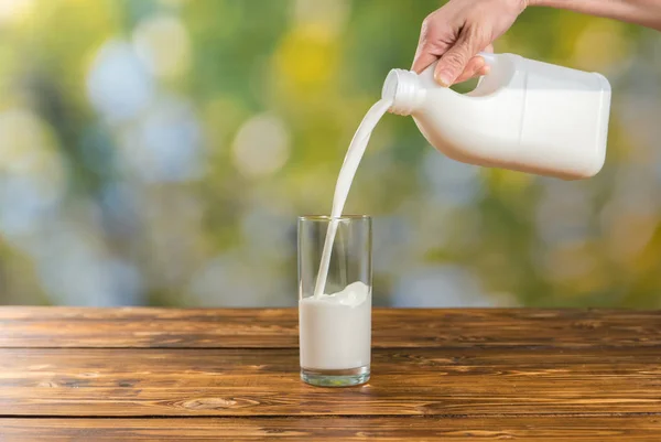Vrouw gieten melk in een glas in de tuin — Stockfoto