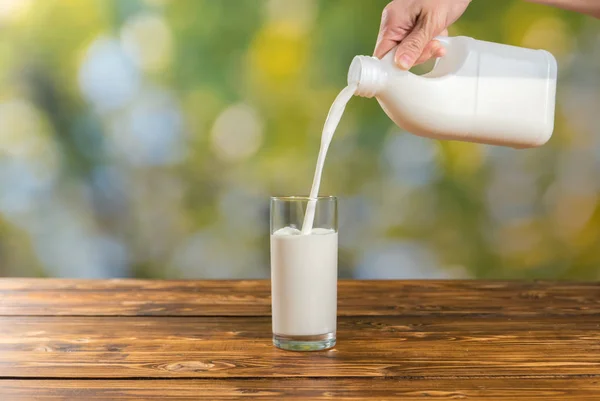 Mujer vertiendo leche fresca en un vaso sobre fondo verde — Foto de Stock