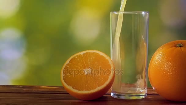 Апельсиновый сок в стакане на естественном зеленом фоне — стоковое видео