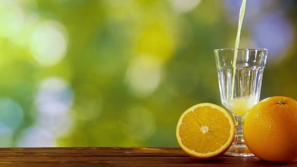 Апельсиновый сок наливать в стекло в саду на фоне природных листьев — стоковое видео