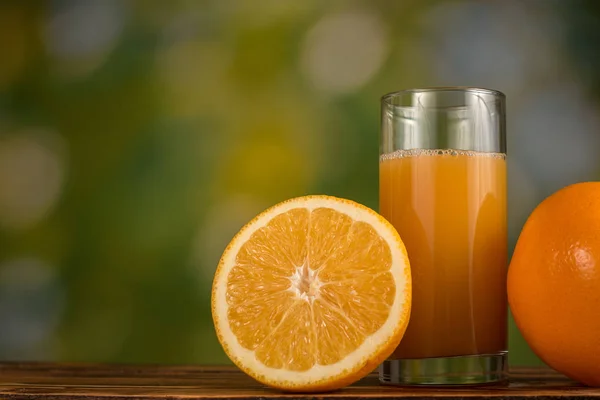 Pomerančová šťáva ve skle a pomeranče na přírodní zelené pozadí Stock Snímky
