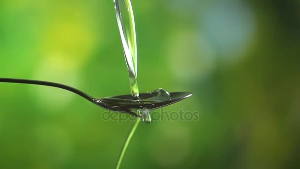 Slow motion close up video of oil being poured in spoon on green background — Stock Video