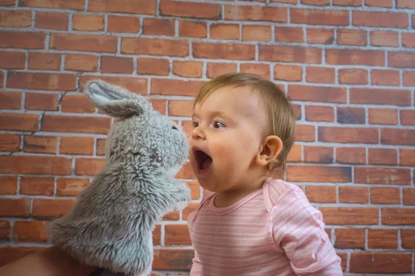 Funny little cute baby girl in pink playing with rabbit on mother hands — Stock Photo, Image