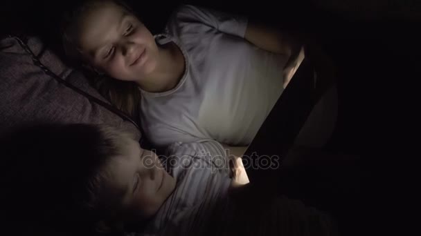 Two kids lying down on the sofa and using tablet pc at night. Slow motion hd video. — Stock Video