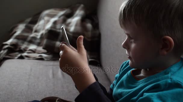 Χαριτωμένο μικρό αγόρι κάθεται στον καναπέ και βλέποντας ταινία στο tablet, βίντεο hd — Αρχείο Βίντεο