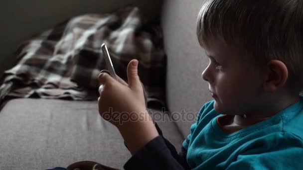 Lindo niño sentado en el sofá y viendo la película en la tableta, video hd — Vídeo de stock