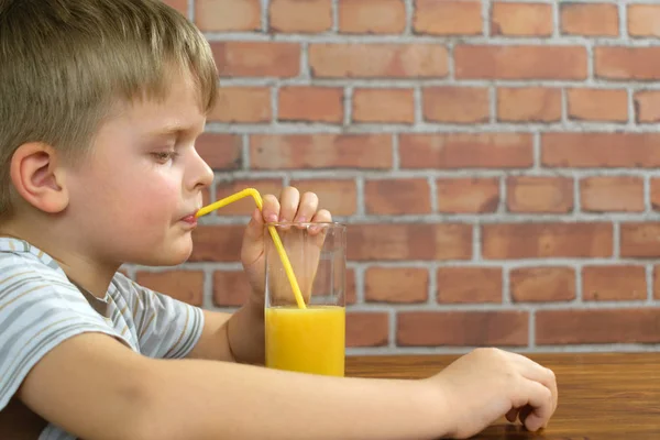 Netter kleiner Junge trinkt Orangensaft aus Stroh — Stockfoto