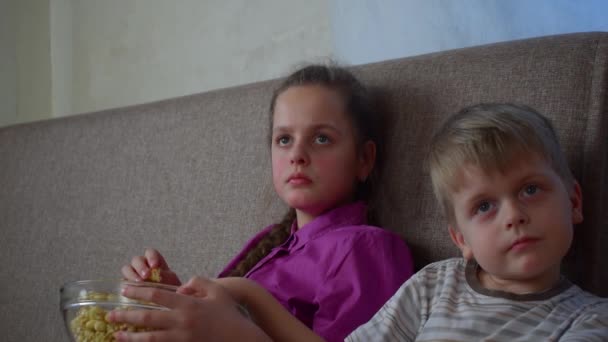 Брат с сестрой смотрят мультик с попкорном — стоковое видео