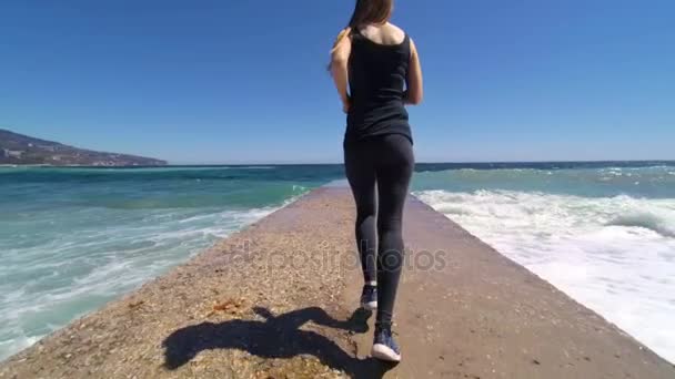 Fille courant le long de la jetée à la mer, jogging le matin, ralenti vidéo HD — Video
